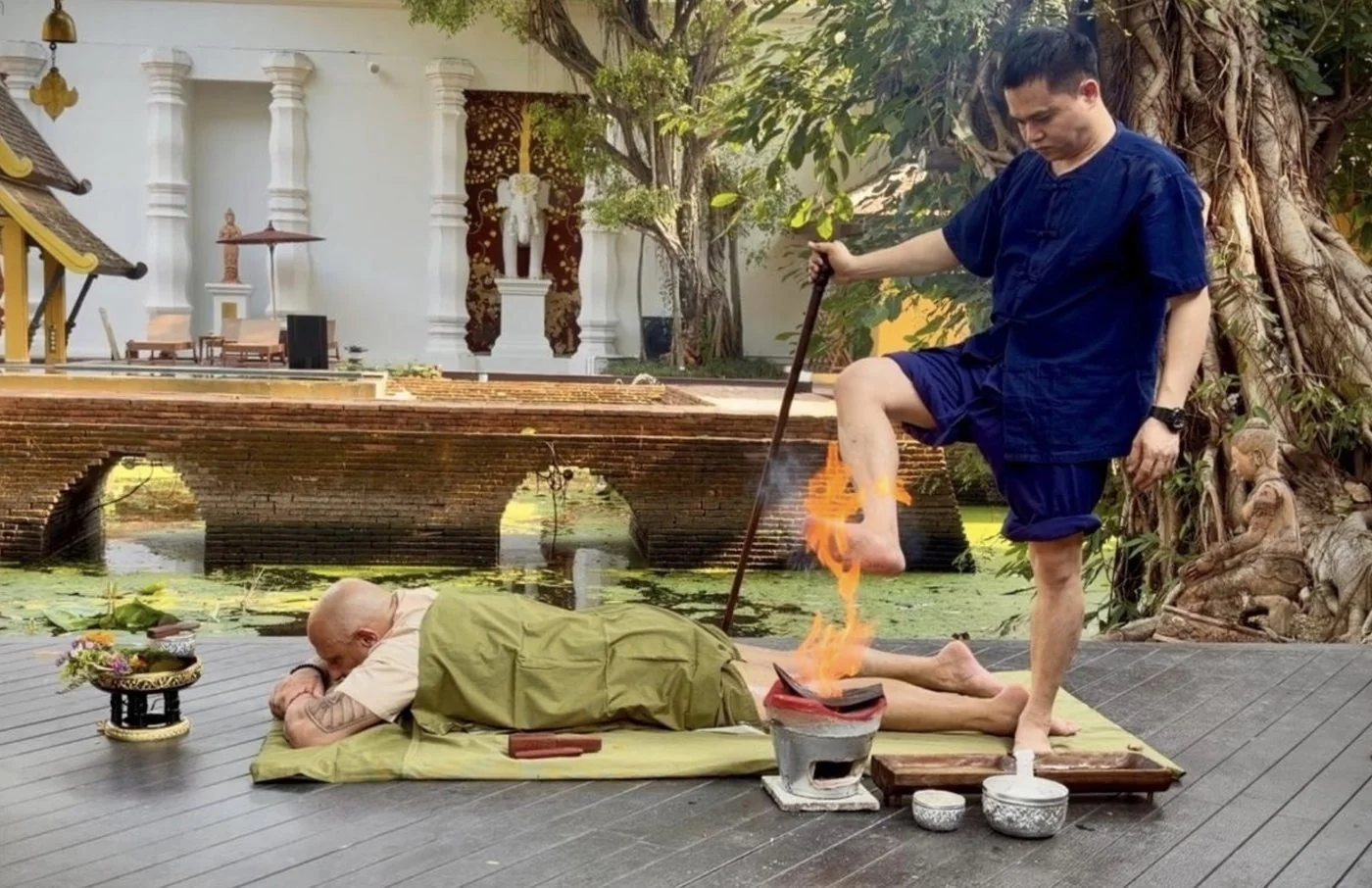 A Yam Khang practitioner in Northern Thailand heating an oiled foot over an open flame before pressing it to a client's back, the traditional Thai fire massage